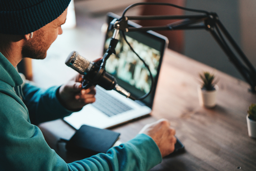 Cheerful host with stubble streaming his audio podcast using microphone and laptop